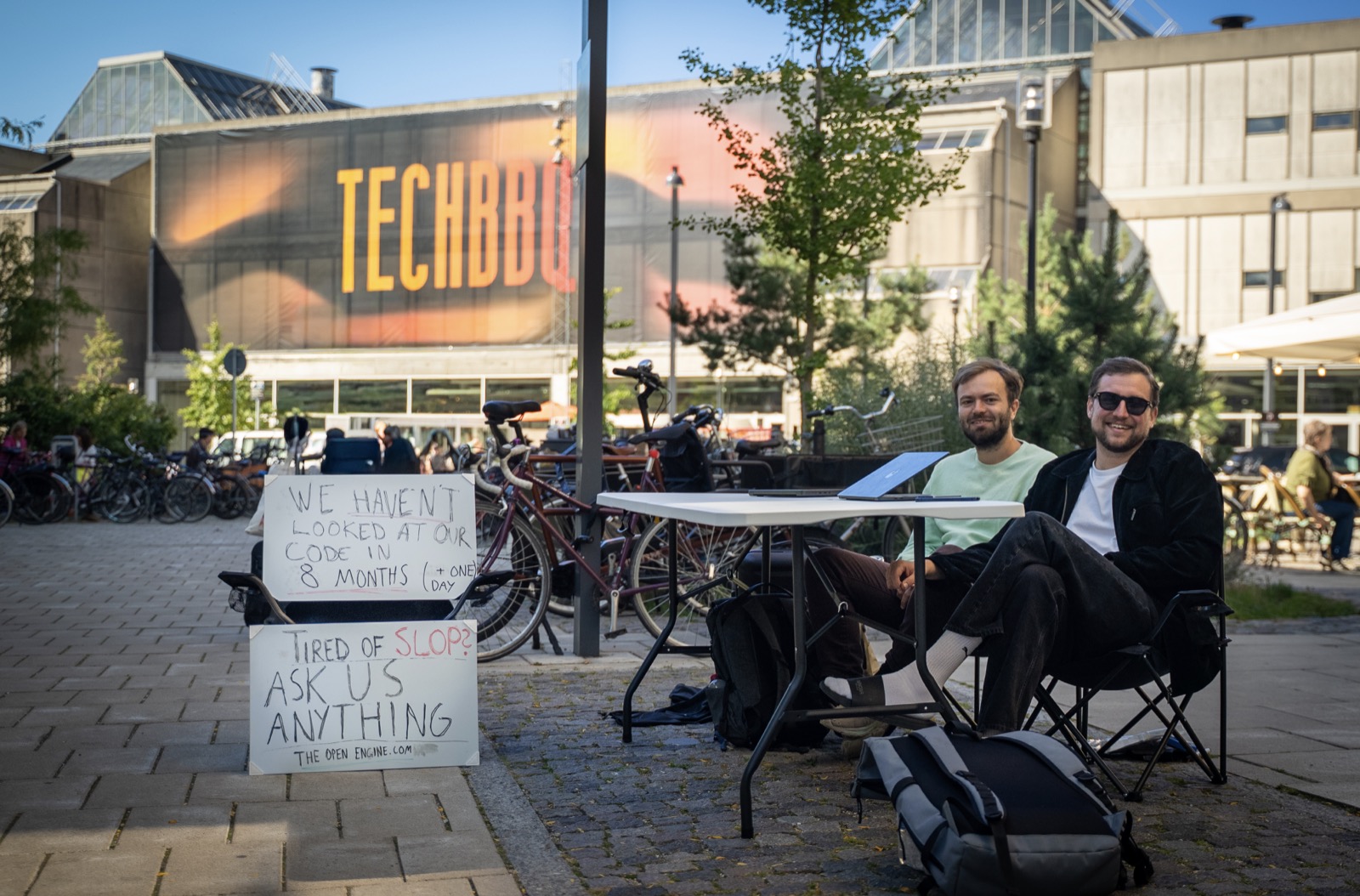 Olle and Eivind at a folding table outside TechBBQ Copenhagen, next to two handwritten signs
